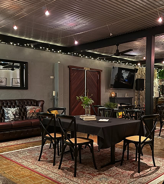 Dining area with a black table and six chairs, a leather sofa, a flat-screen TV, a plant, and decorative string lights.
