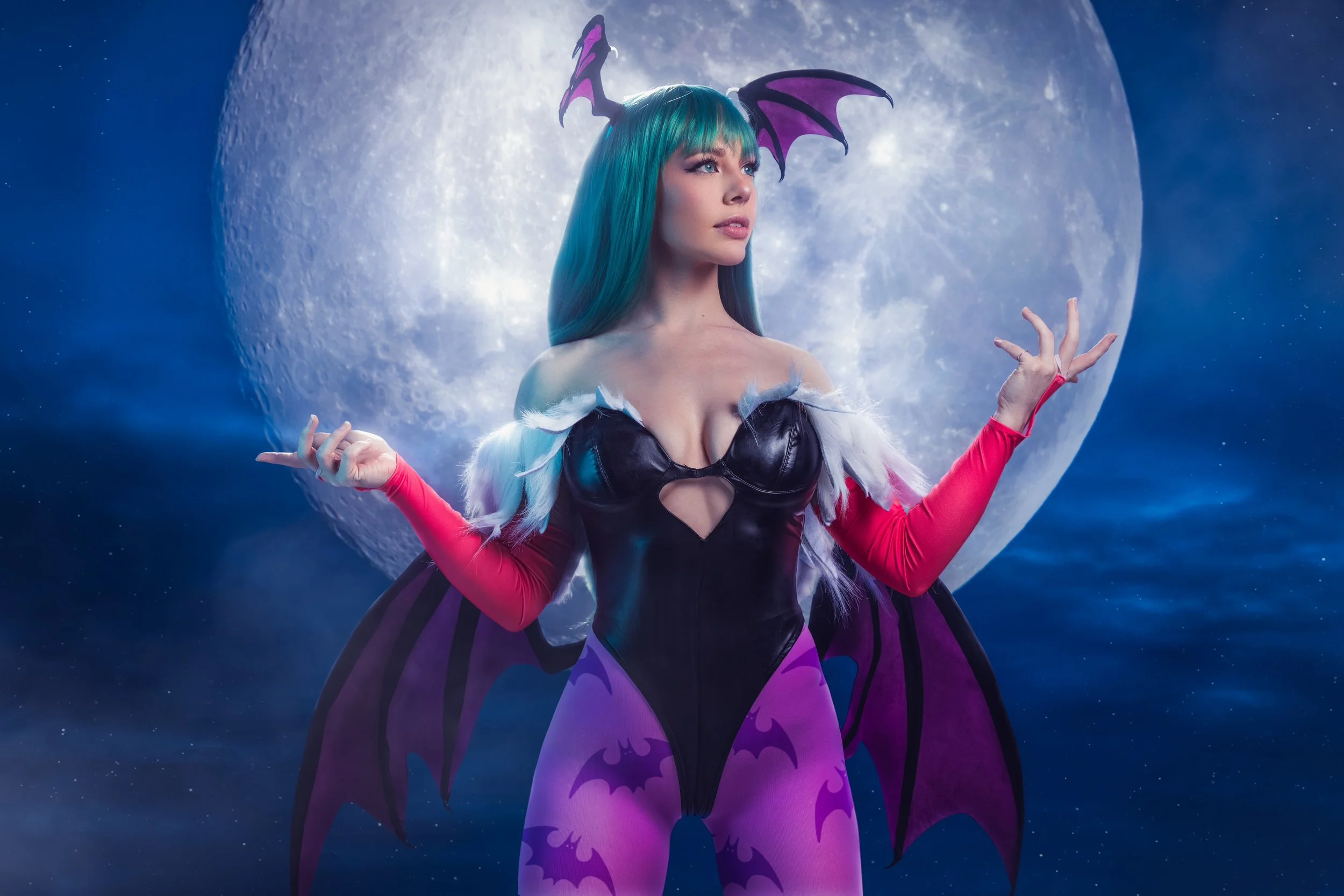 A woman dressed as a fantasy character with dragon wings, with blue hair and purple horns, standing in front of a large, bright moon.