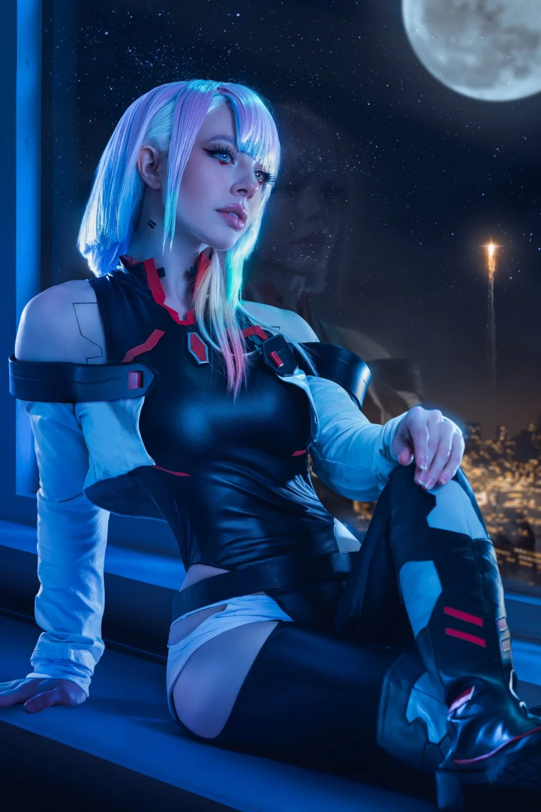 A woman with pastel multicolored hair and futuristic makeup, dressed in a sci-fi outfit, sitting indoors with a city skyline and moon visible through a window at night.