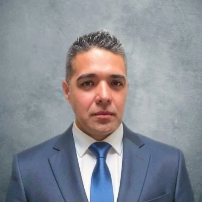 Portrait of a man in a suit and tie standing against a gray background.