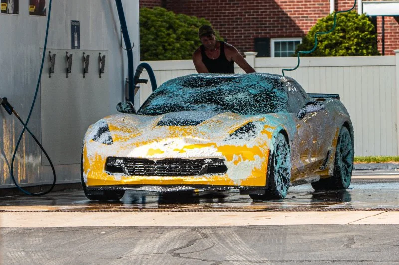 Customer washing a sports car with foam at a Franklin Car Wash self-service bay