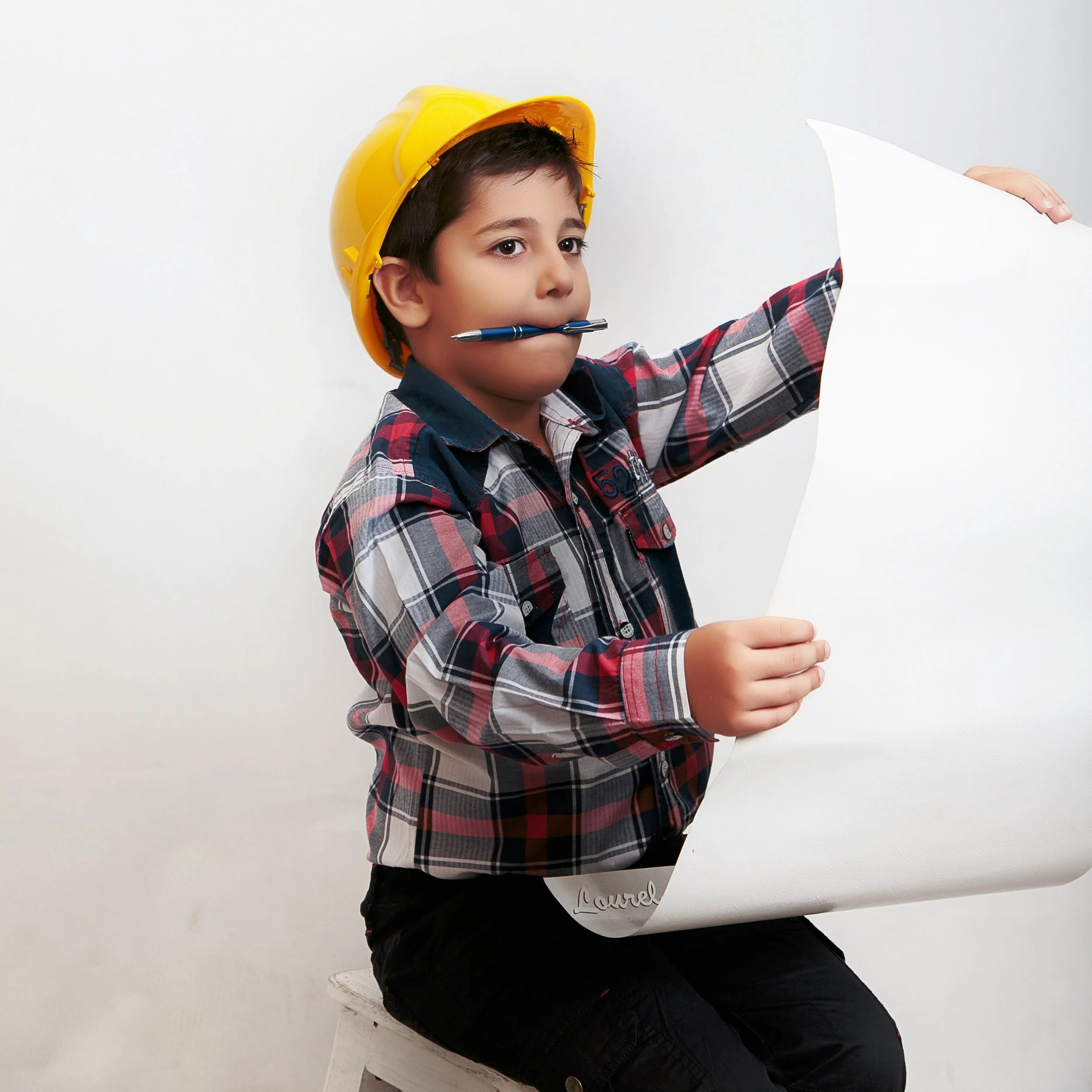 Boy holding construction blueprints with a pen in his mouth