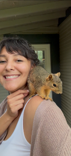 A woman smiling with a squirrel perched on her shoulder.