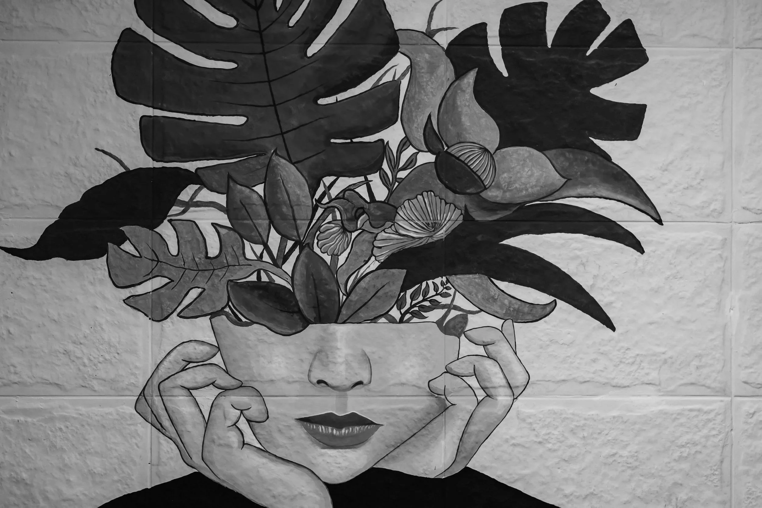 Black and white illustration of a woman's face with her eyes closed, hands gently holding her head, surrounded by large tropical leaves and flowers.