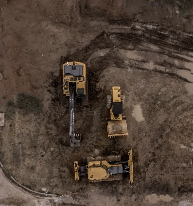 Aerial view of three yellow construction excavators working on a dirt site.