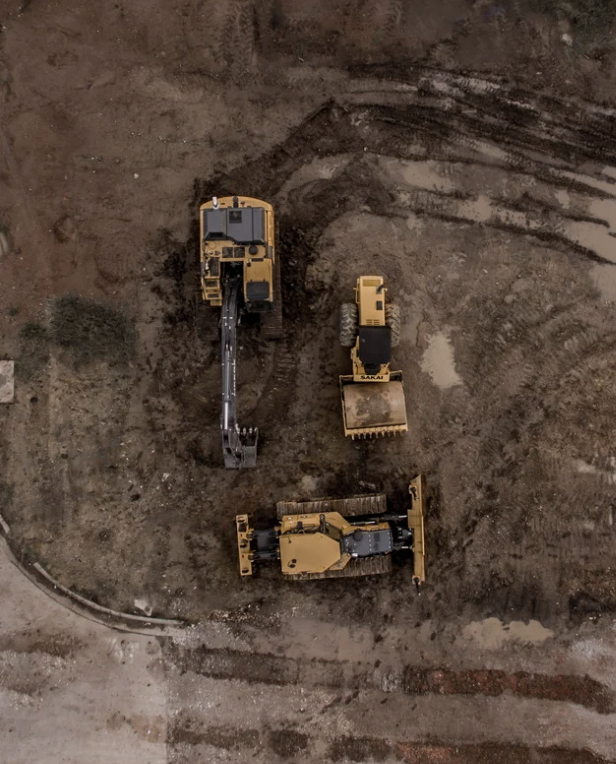 Three yellow construction vehicles working on a dirt terrain. One excavator, a small loader, and a bulldozer.