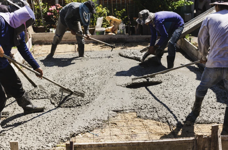 Workers pouring and leveling concrete on a construction site outdoors.