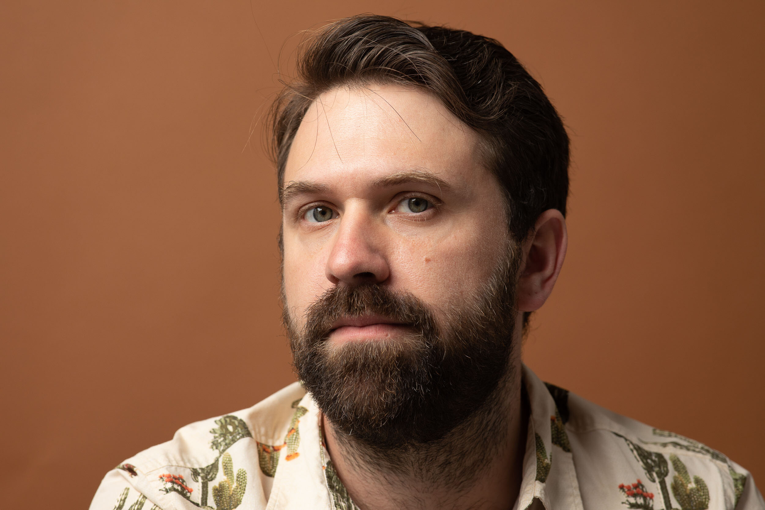 Portrait of a bearded man in a cactus print shirt against a brown background.