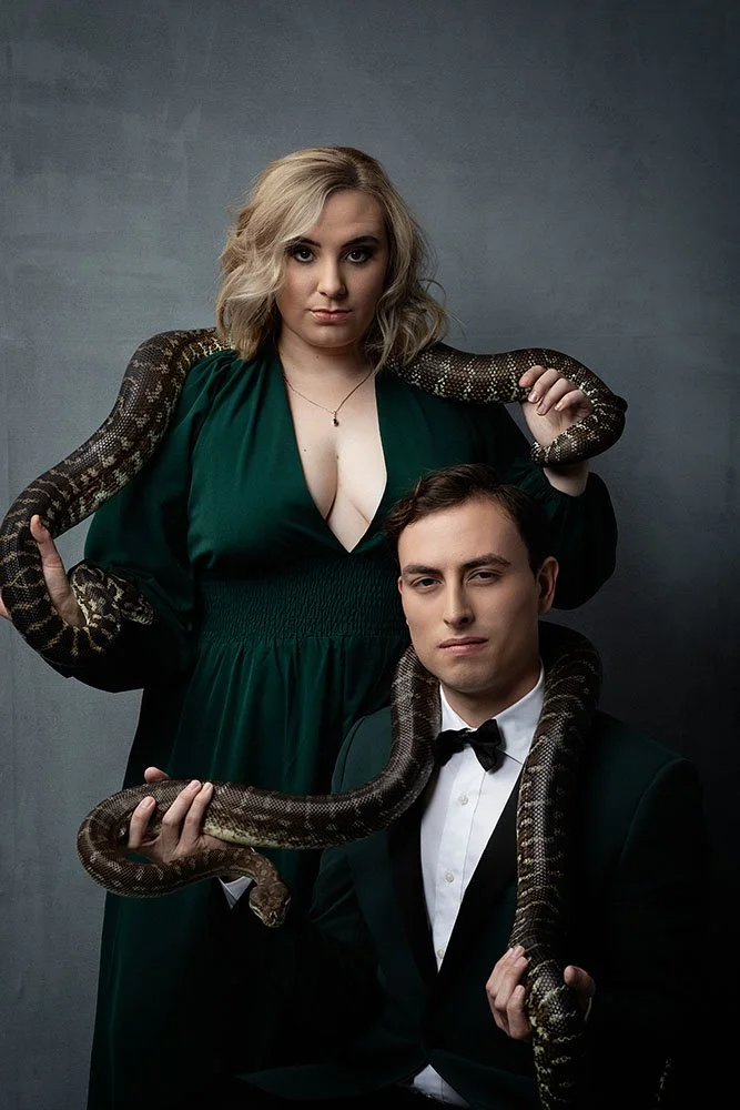 A woman in a green dress and a man in a tuxedo holding a large snake.