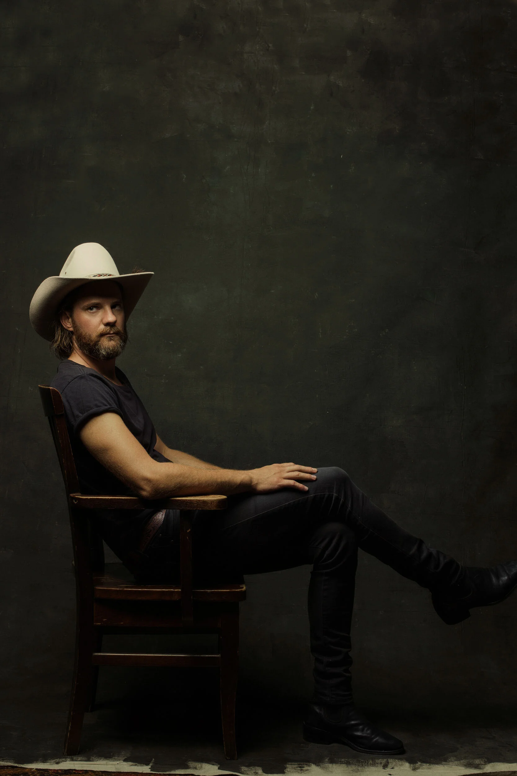 Ben Mastwick cowboy hat sitting on wooden chair against dark background.