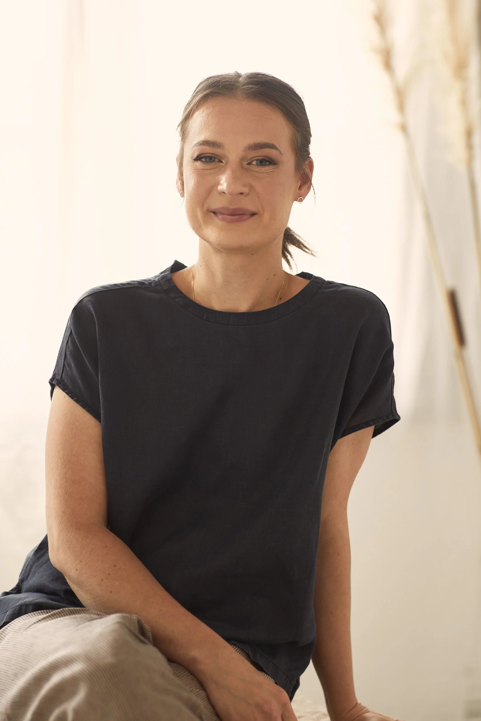 Smiling person sitting indoors, wearing a dark shirt, neutral background.