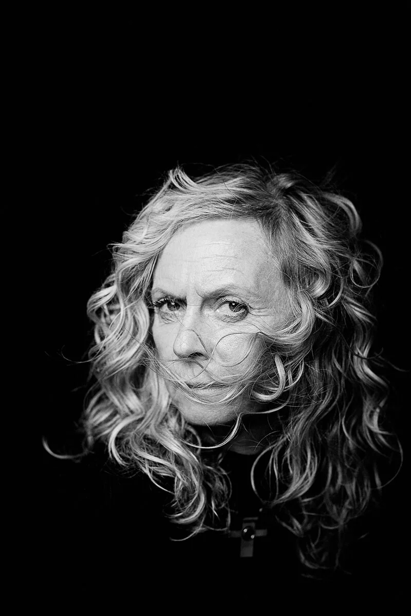 Black and white portrait of a person with curly hair, partially covering their face.