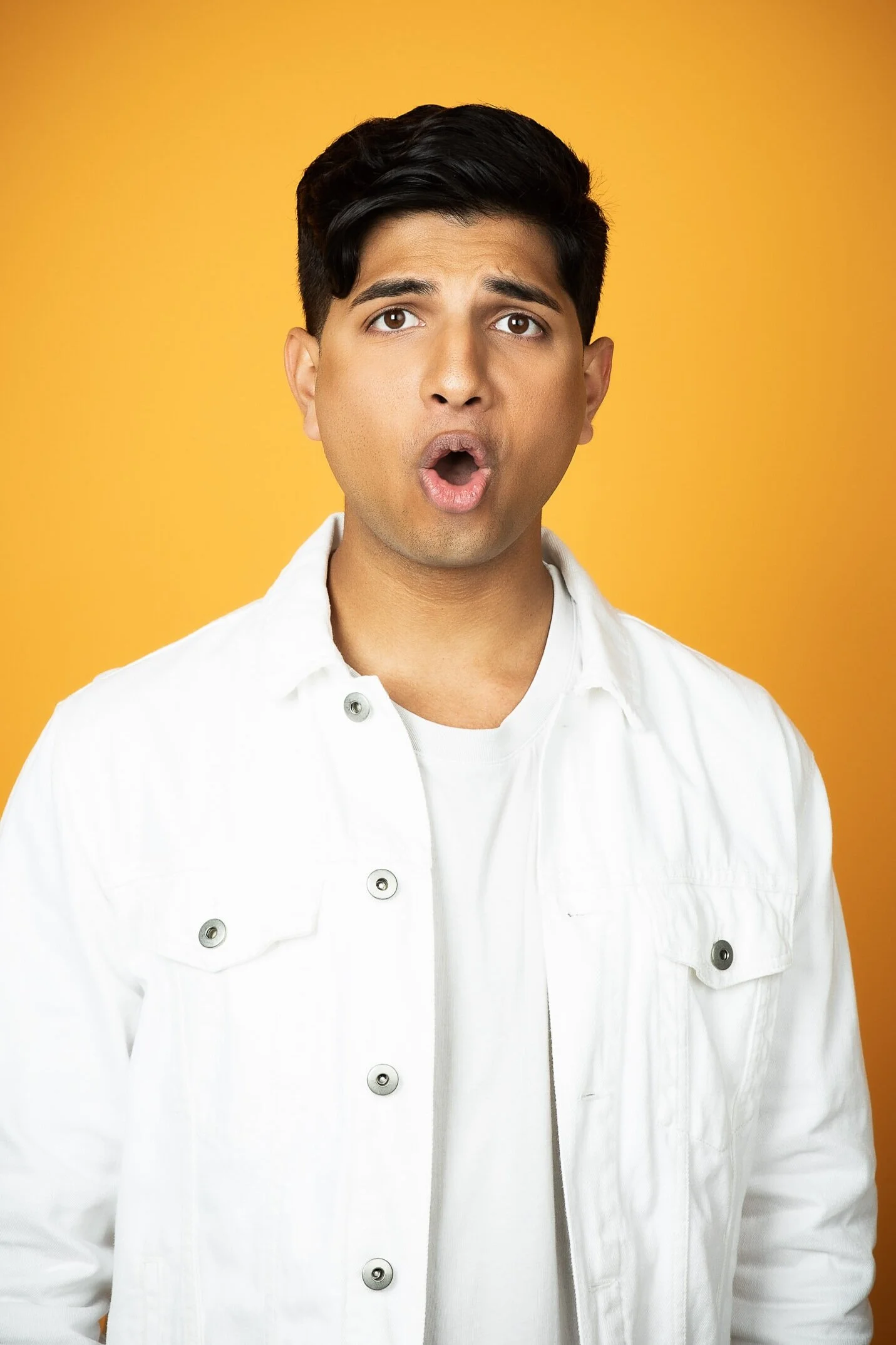 Man in white jacket against orange background, looking surprised.