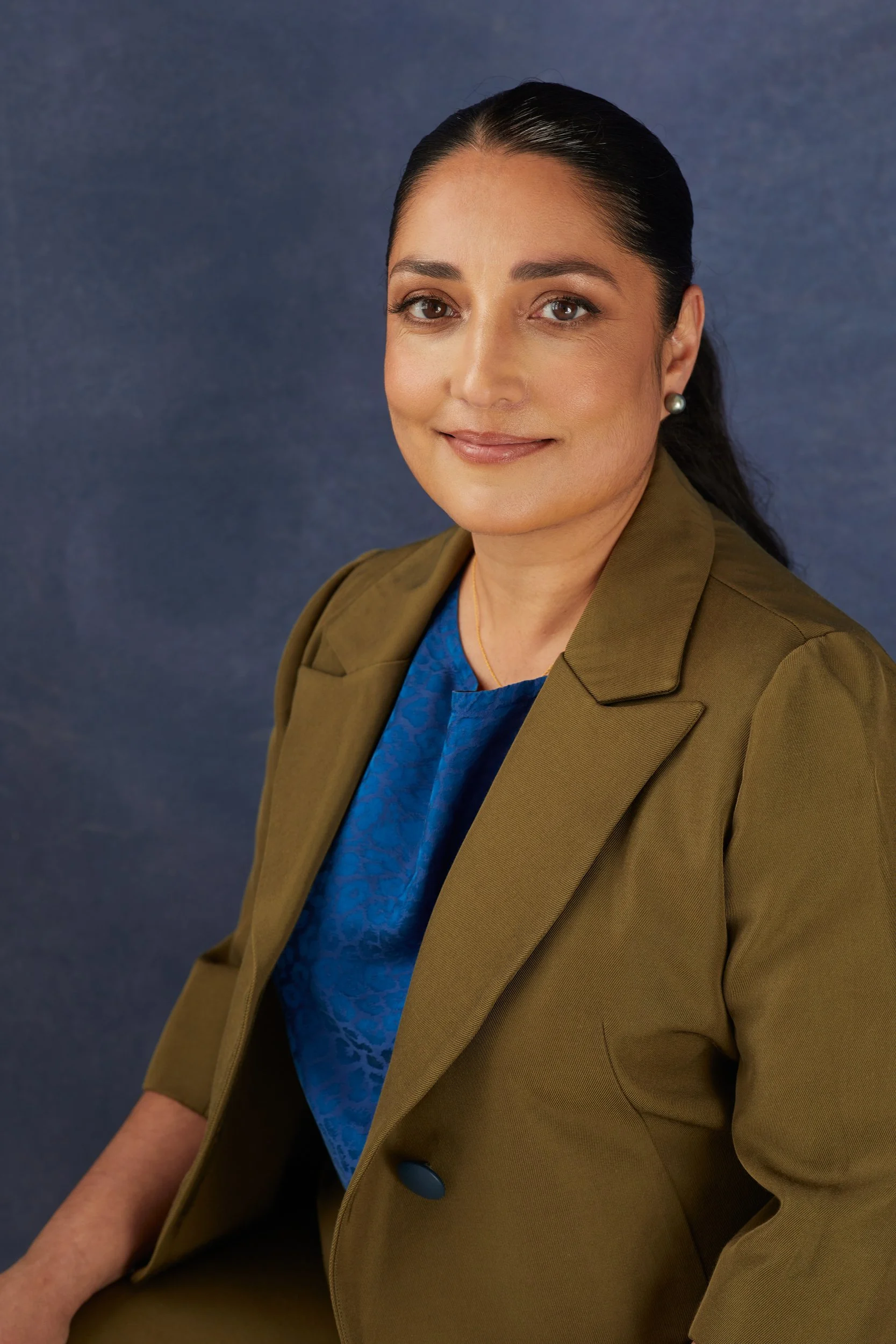 Person wearing a green blazer and blue shirt in front of a blue background