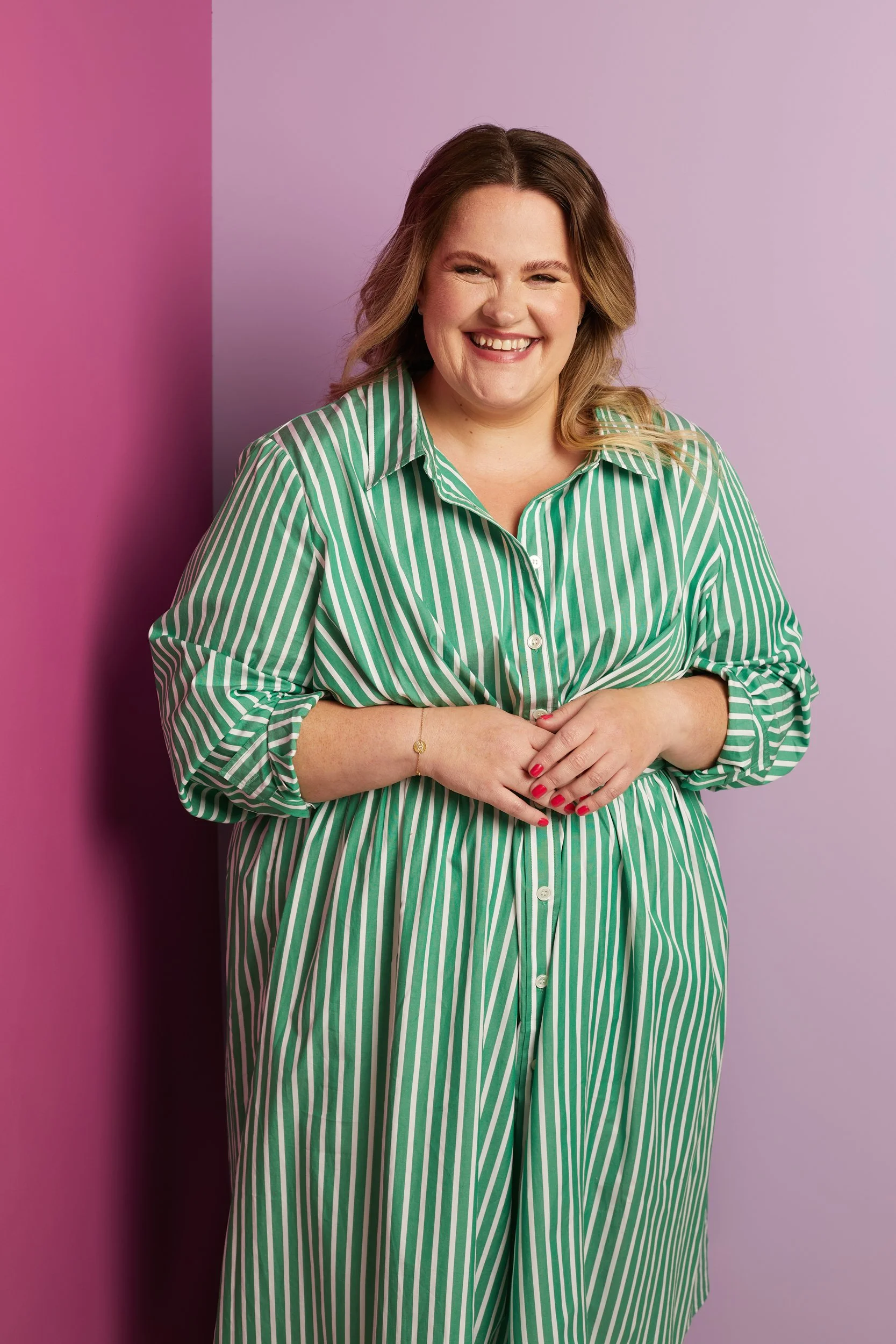 Smiling person in a green and white striped dress against a pink and lavender background.