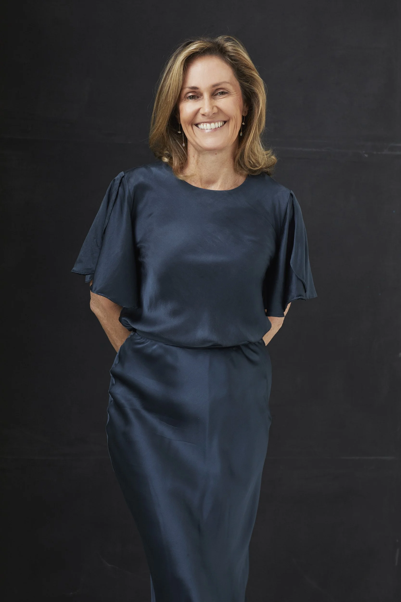 Smiling woman in dark blue dress against black background.