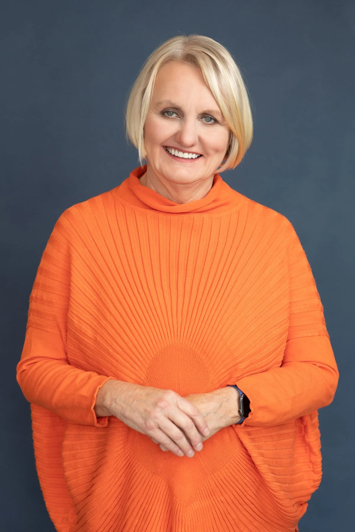 Person wearing an orange sweater against a blue background.