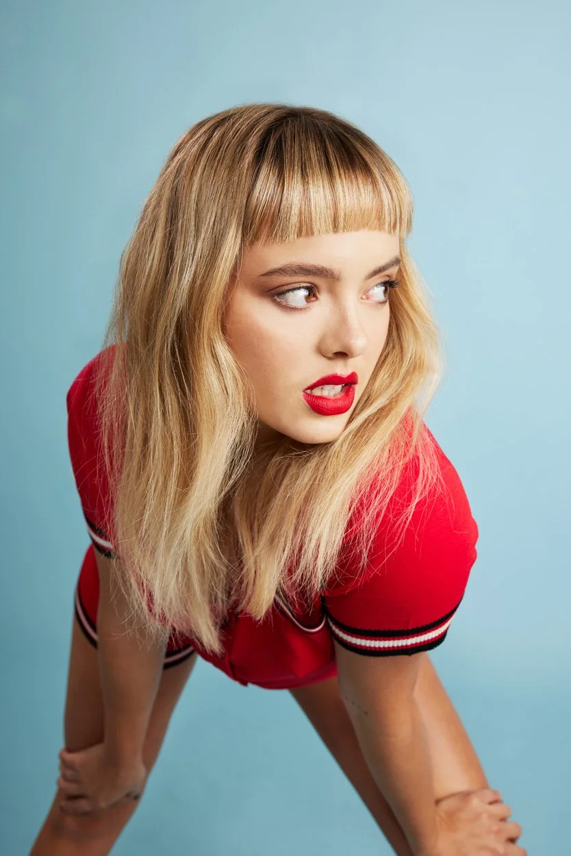 Woman with blonde hair and red lipstick in a red top against a blue background.