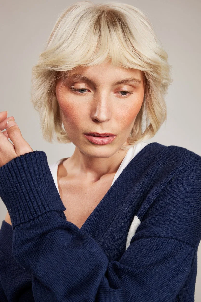 Person with short blonde hair wearing a navy blue sweater.