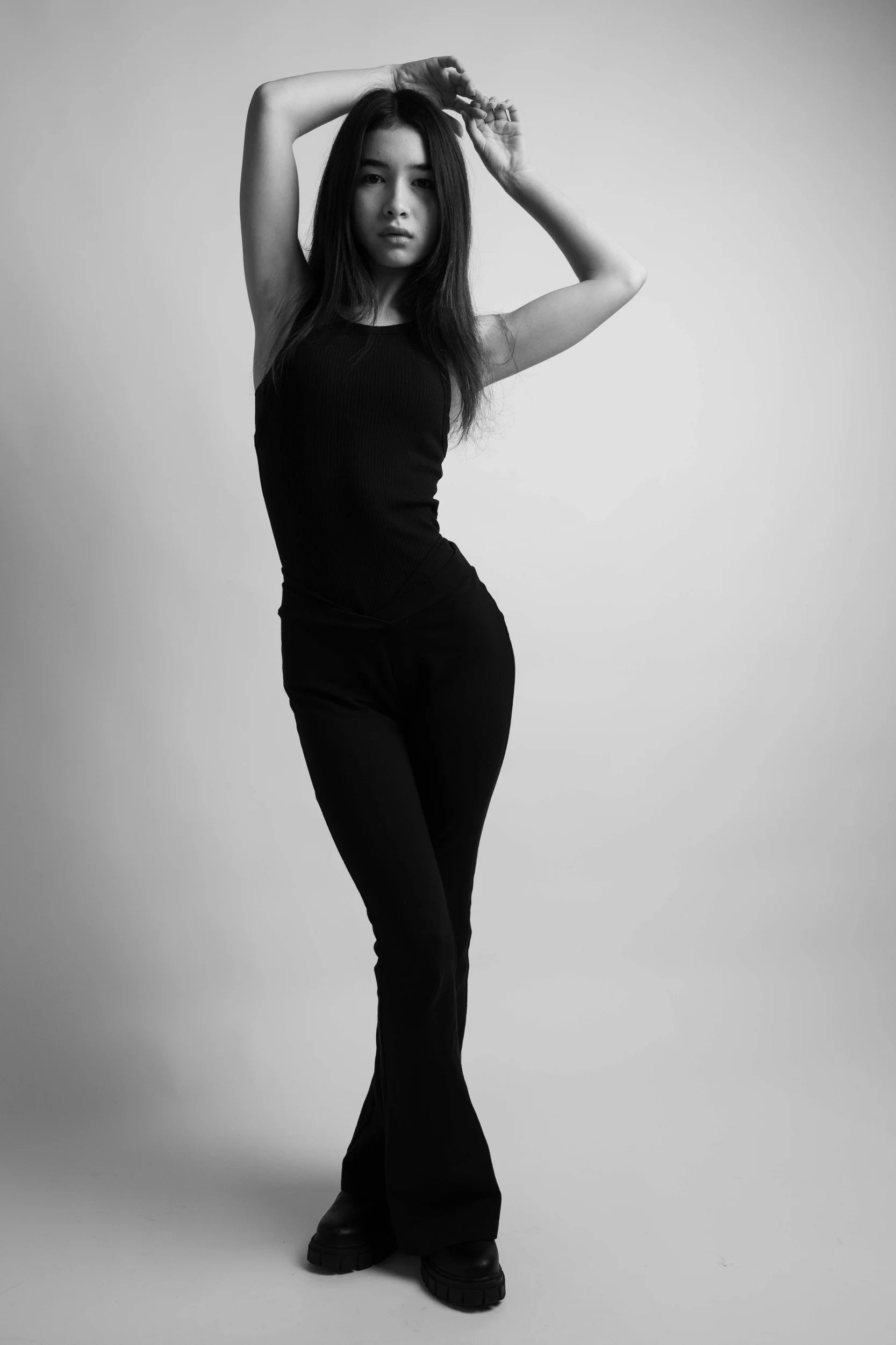 Black and white photo of a person in a black outfit striking a pose with arms raised