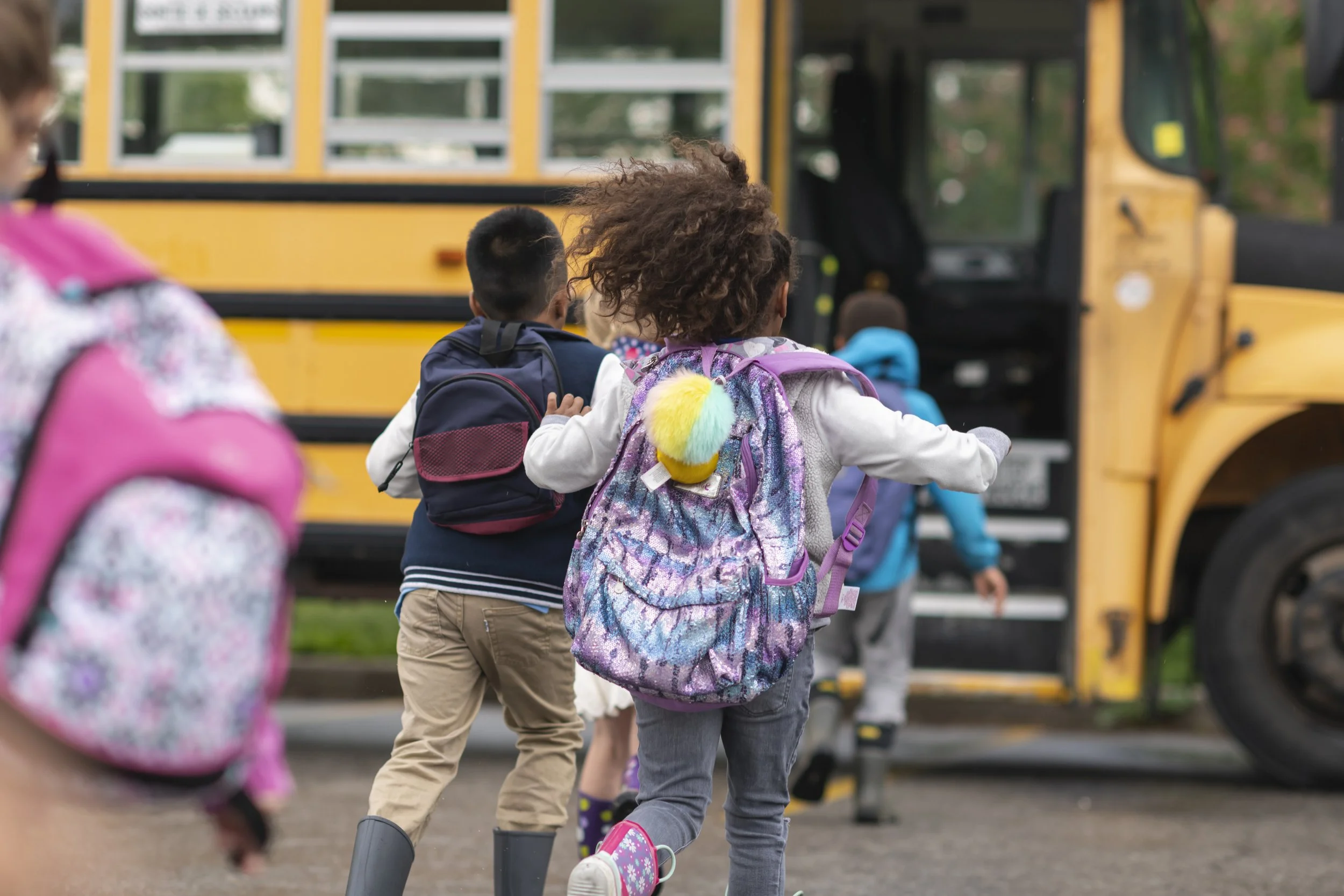Children boarding a yellow school bus at a school pickup area.