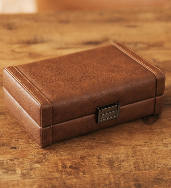 A rectangular brown leather cigar travel case with a metal latch on a wooden surface. Sold at Outlaw Vapor in Preston and Malad, Idaho.