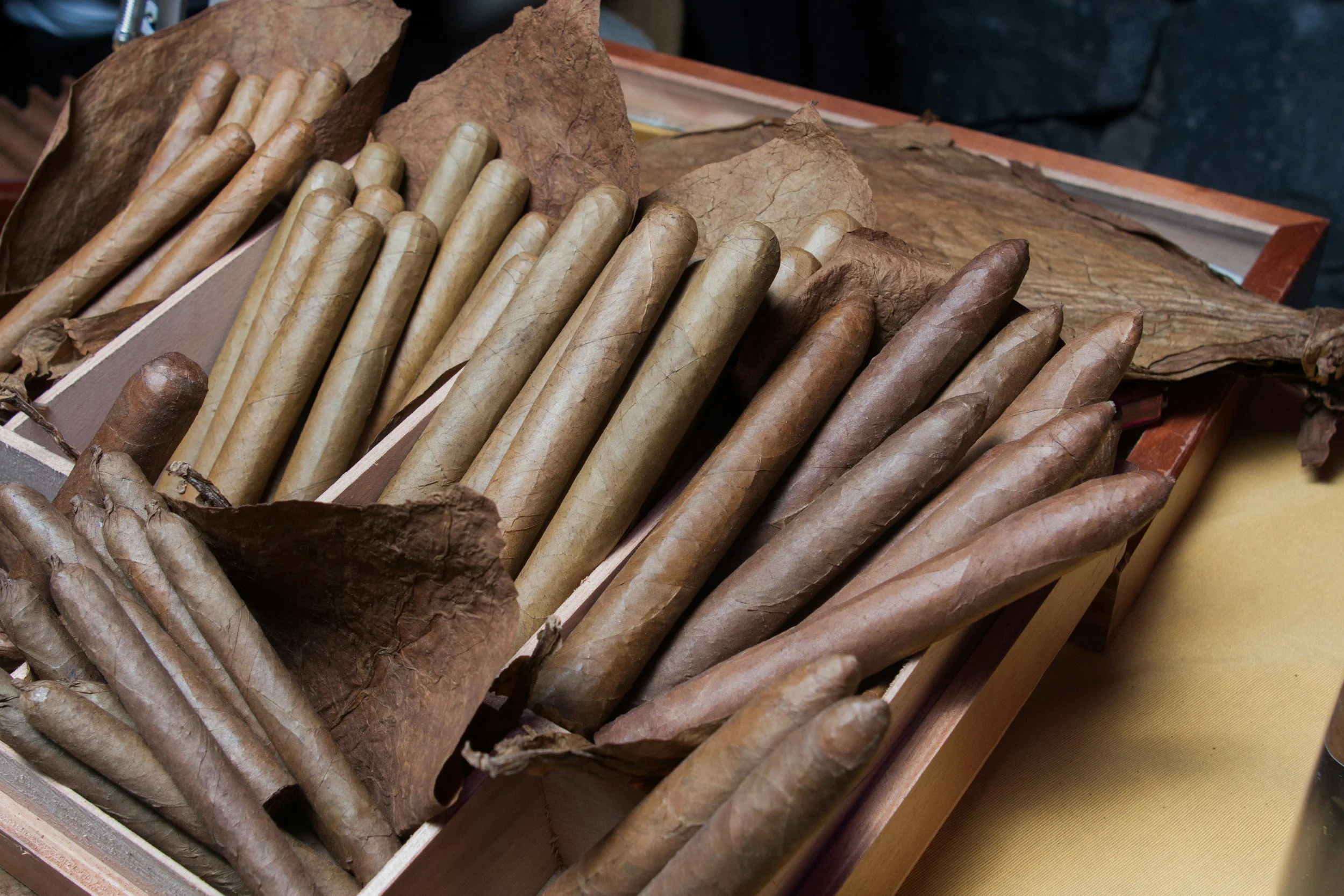 A wooden box containing tightly wrapped cigars resting on large dry leaves. Sold at Outlaw Vapor in Preston and Malad, Idaho.