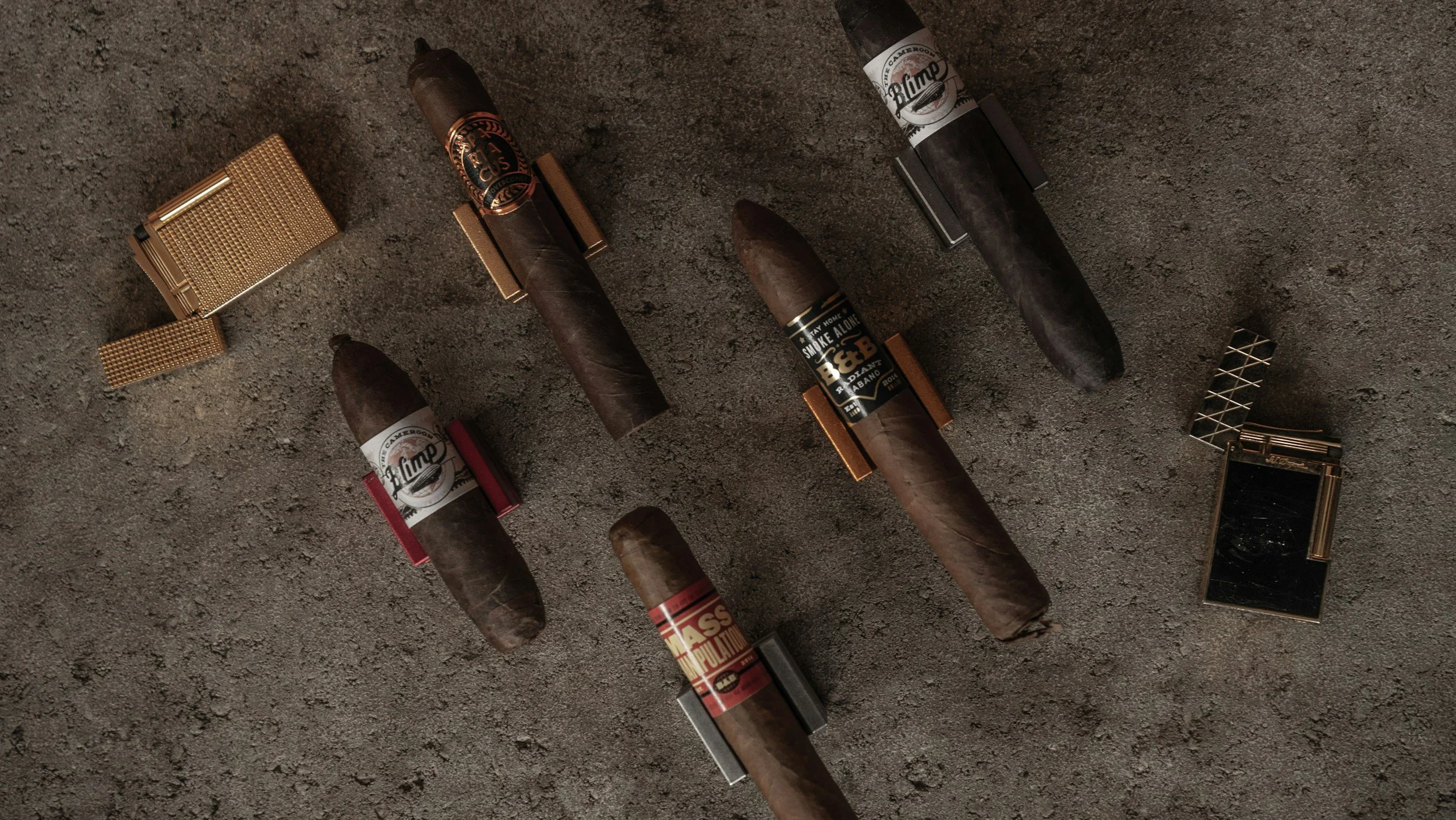 Multiple cigars with bands and lighters on a textured surface. Sold at Outlaw Vapor in Preston and Malad, Idaho.