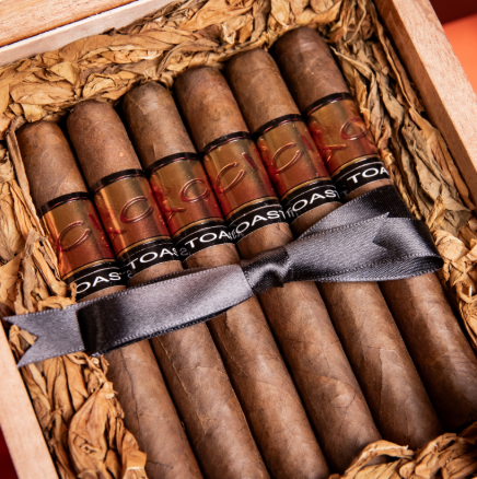A box of Drew Estate six cigars tied with a black ribbon inside a wooden box lined with crumpled paper. Sold at Outlaw Vapor in Preston and Malad, Idaho.