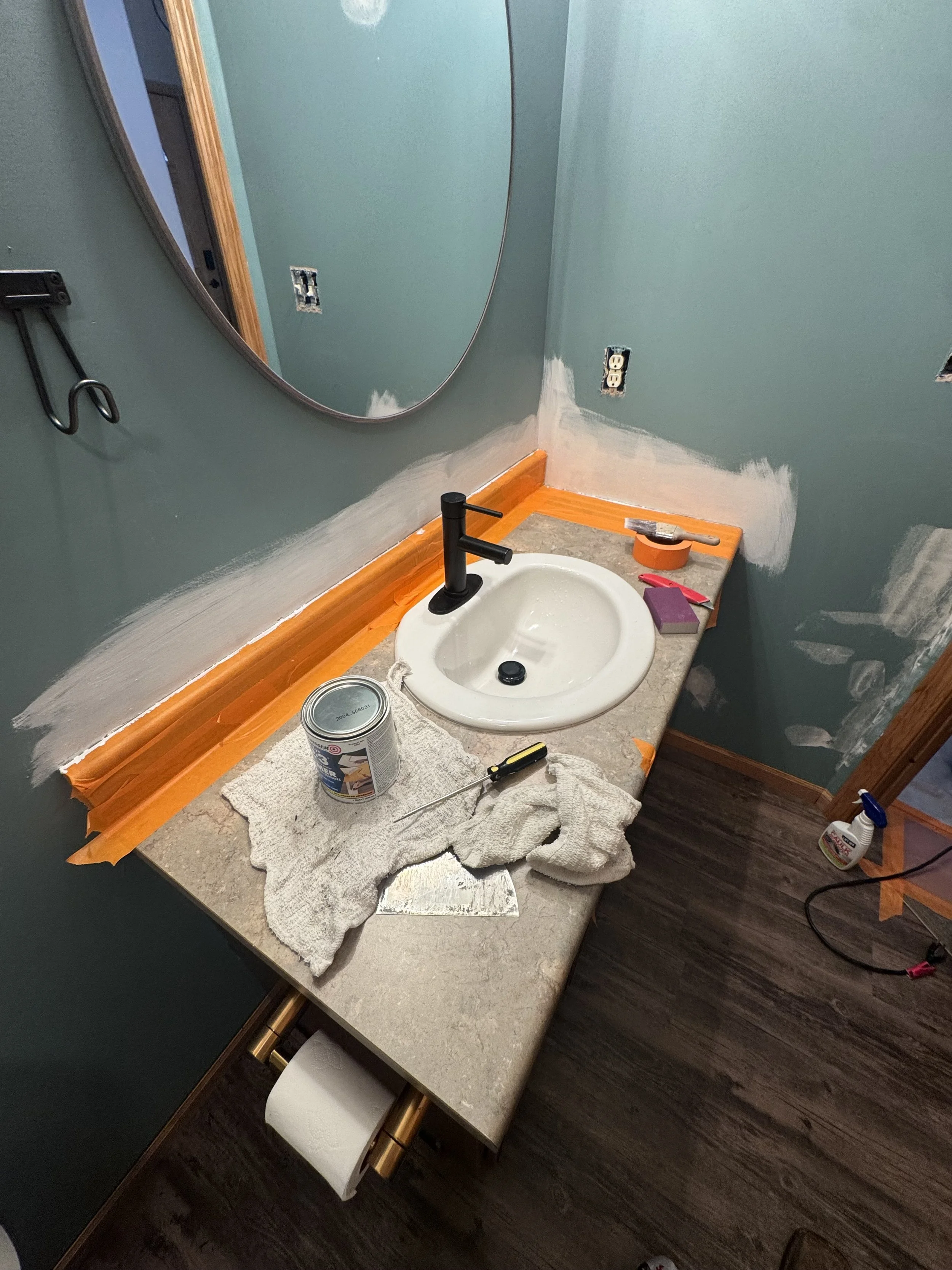 Bathroom vanity with a mirror, partially painted wall, a sink, electrical outlets, and tools including a can of paint, a screwdriver, and a paint roller.