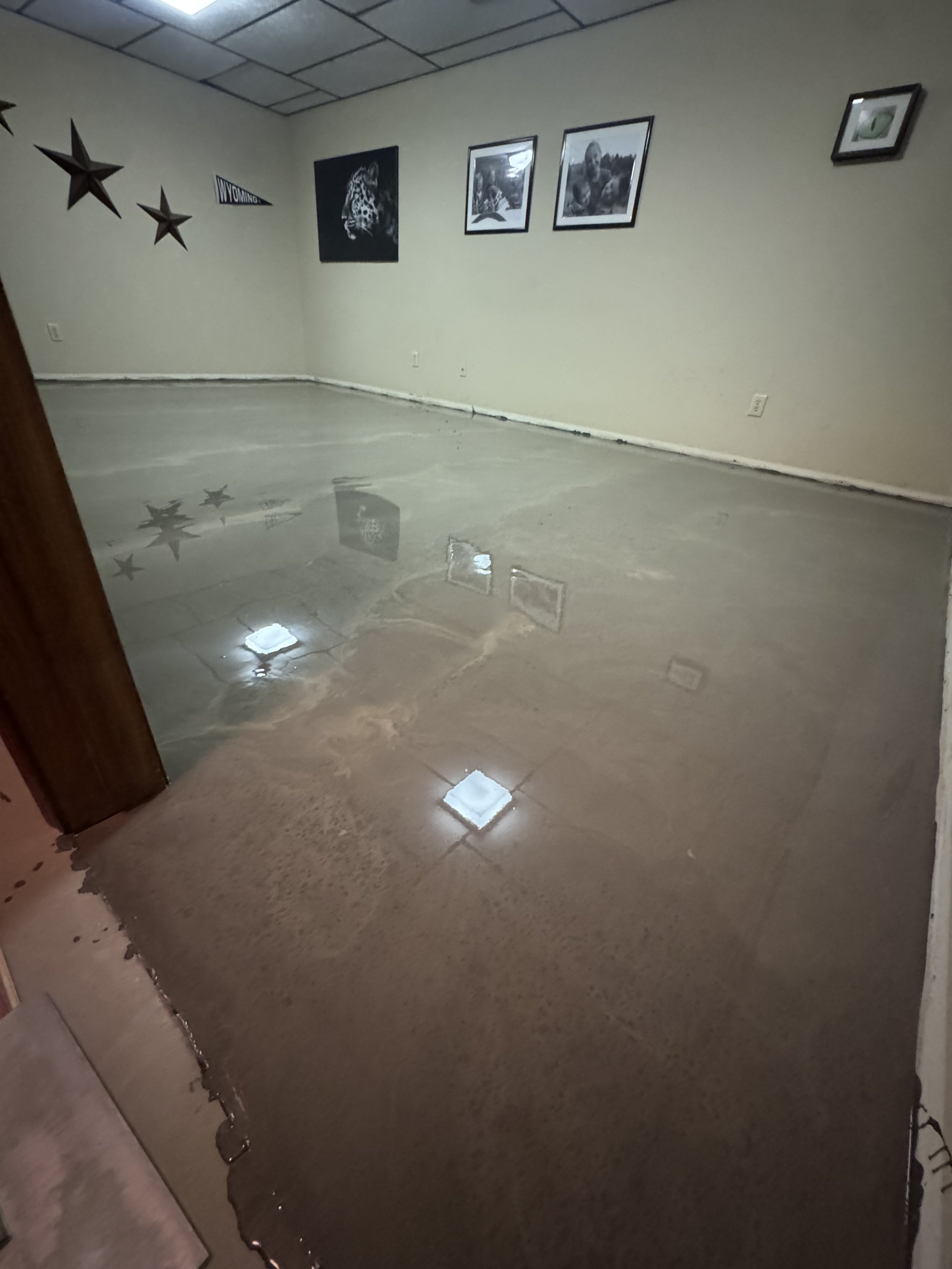 Empty room with beige walls, decorated with framed photos, star-shaped wall decorations, a Wyoming pennant, and reflections of ceiling lights on a polished floor.
