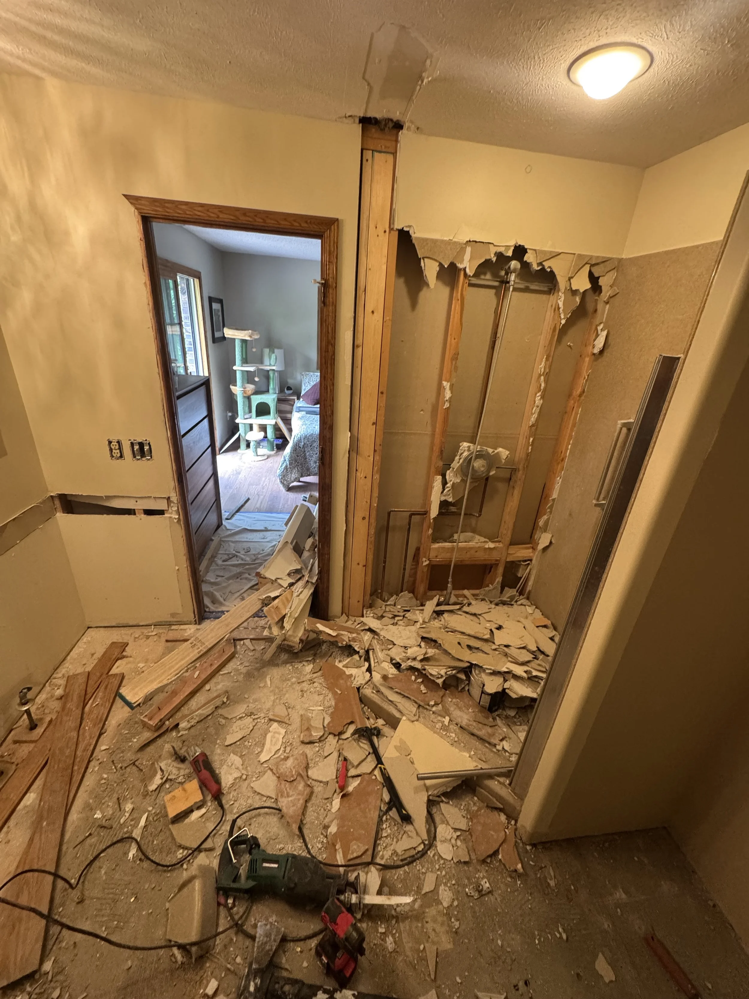Photo of a room undergoing demolition with drywall torn down, insulation exposed, and construction tools on the floor.