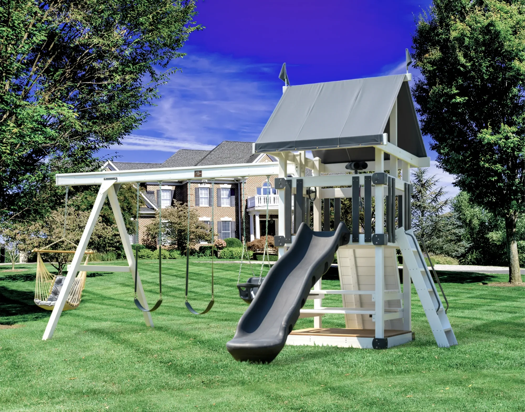 A backyard playground with a swing set, slide, and a porch swing in a grassy area, surrounded by trees and a brick house in the background, under a blue sky.