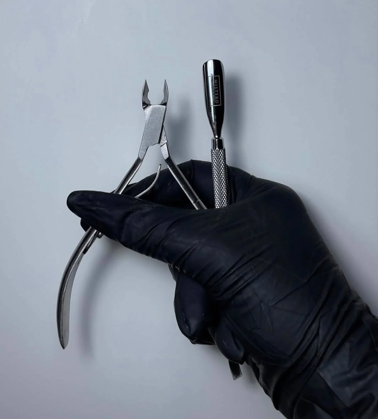 A hand wearing a black glove holding a pair of dental or surgical forceps and a scalpel against a plain white background.
