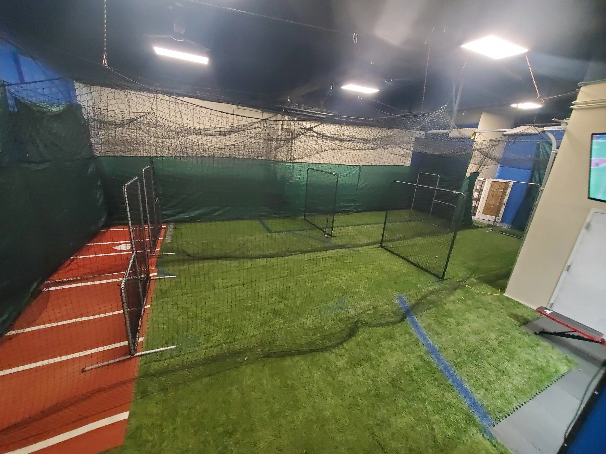 Indoor sports training facility with artificial turf, a batting cage with a net, and sideline markings for sports activities.