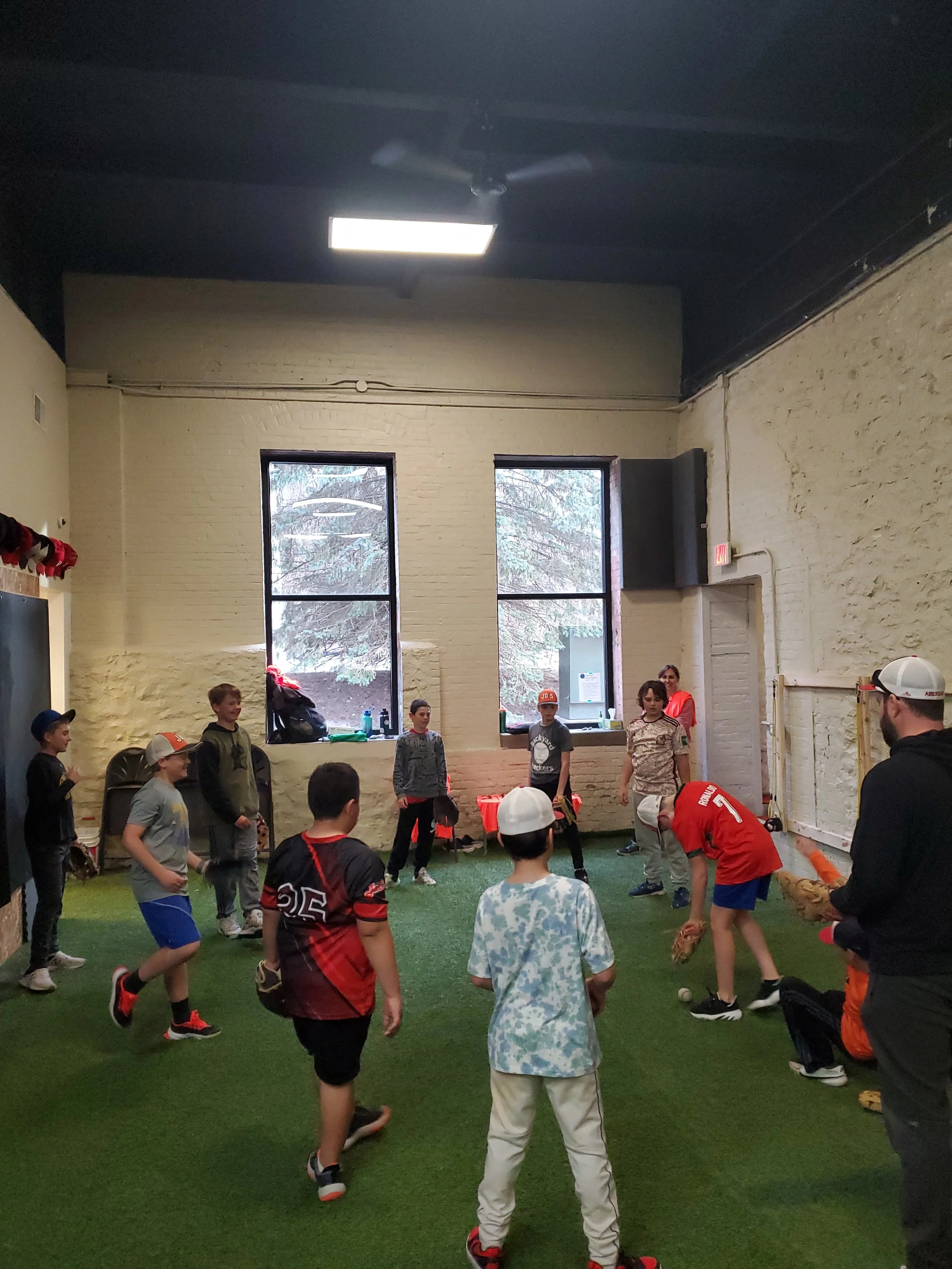 Kids playing football practice indoors on artificial turf with coaches supervising.