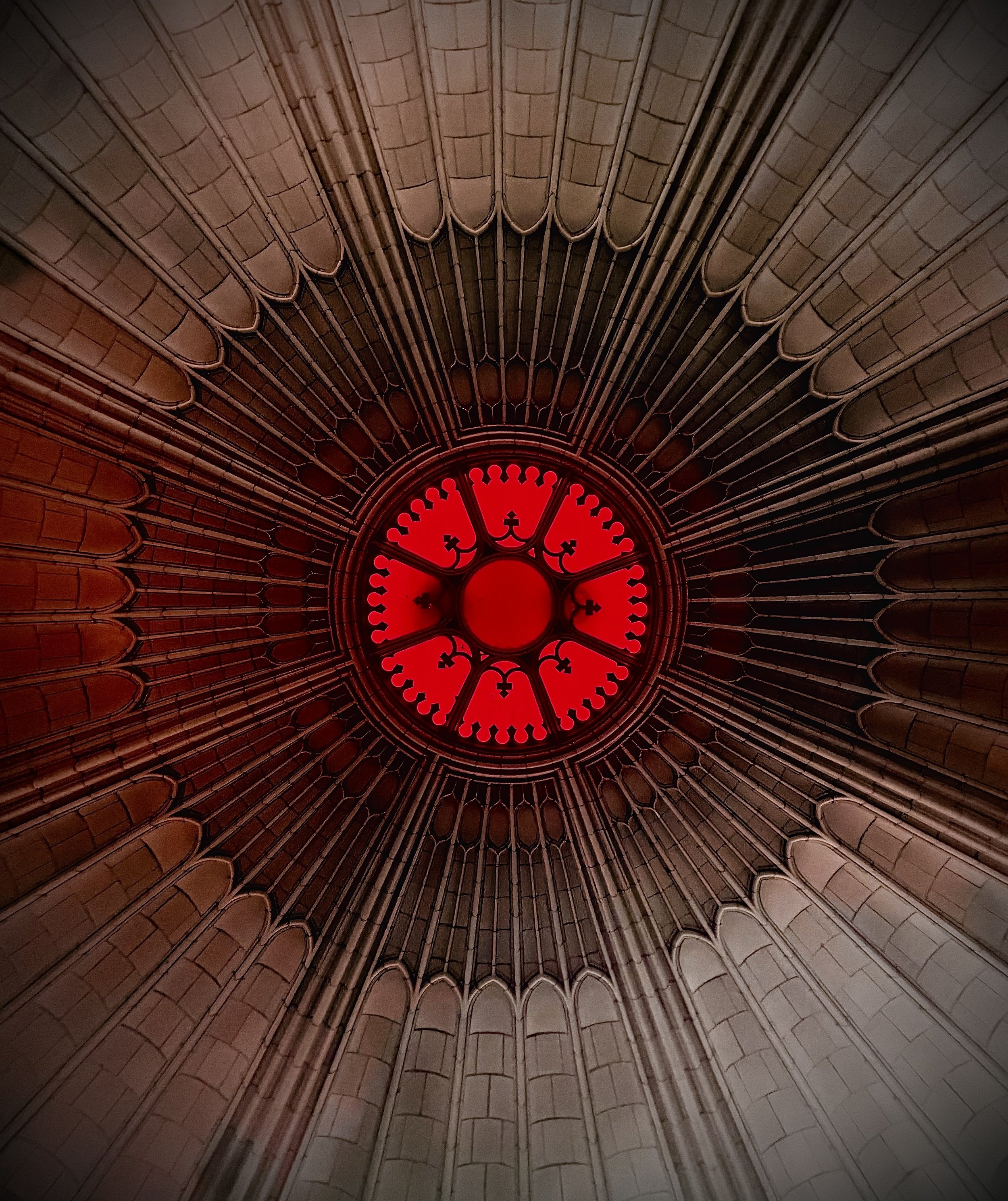 Looking up at a vaulted, intricate Gothic cathedral ceiling with a glowing red clock at the center.