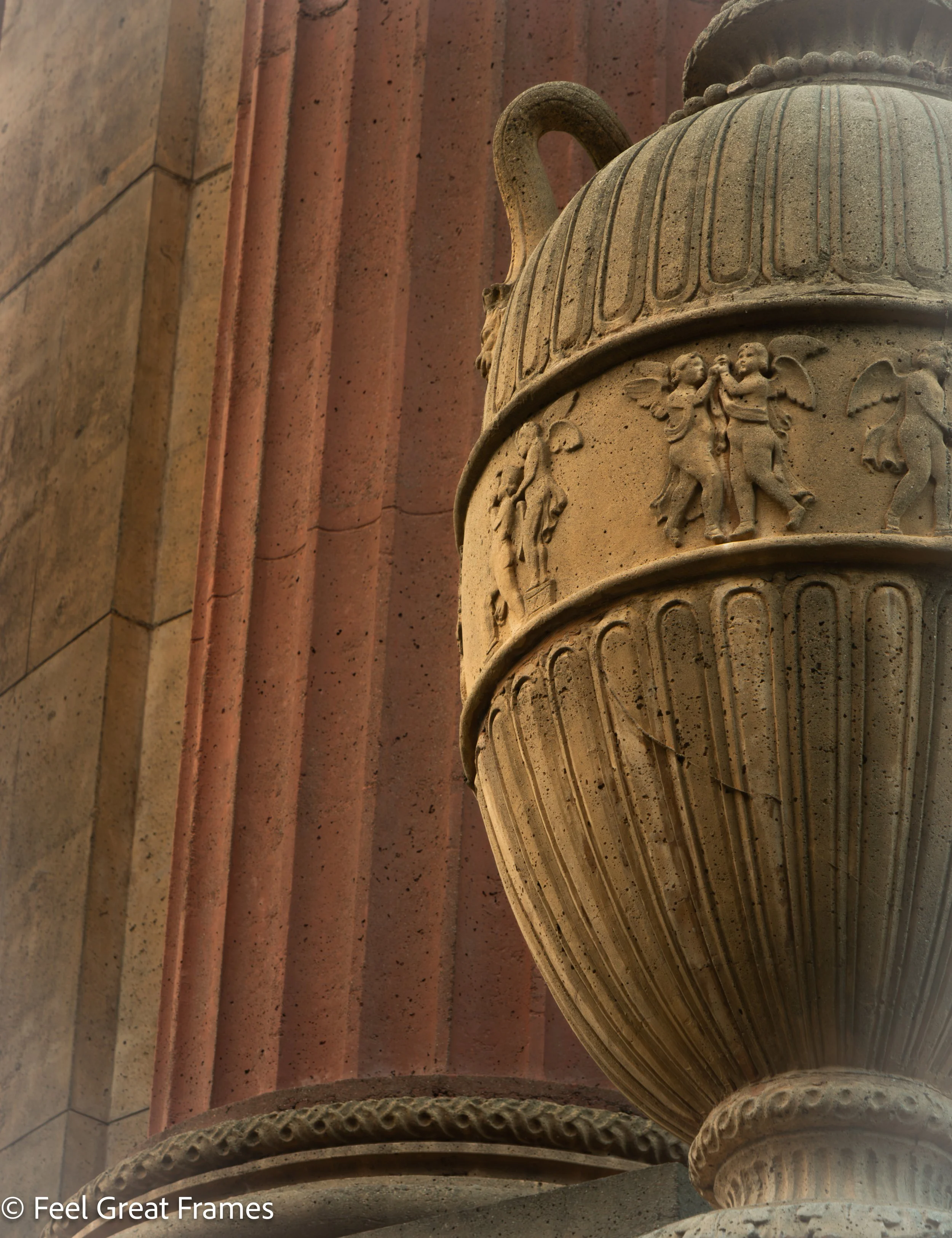 Close-up of a carved stone column with decorative patterns, set against a background of red and beige stone wall with ledges.