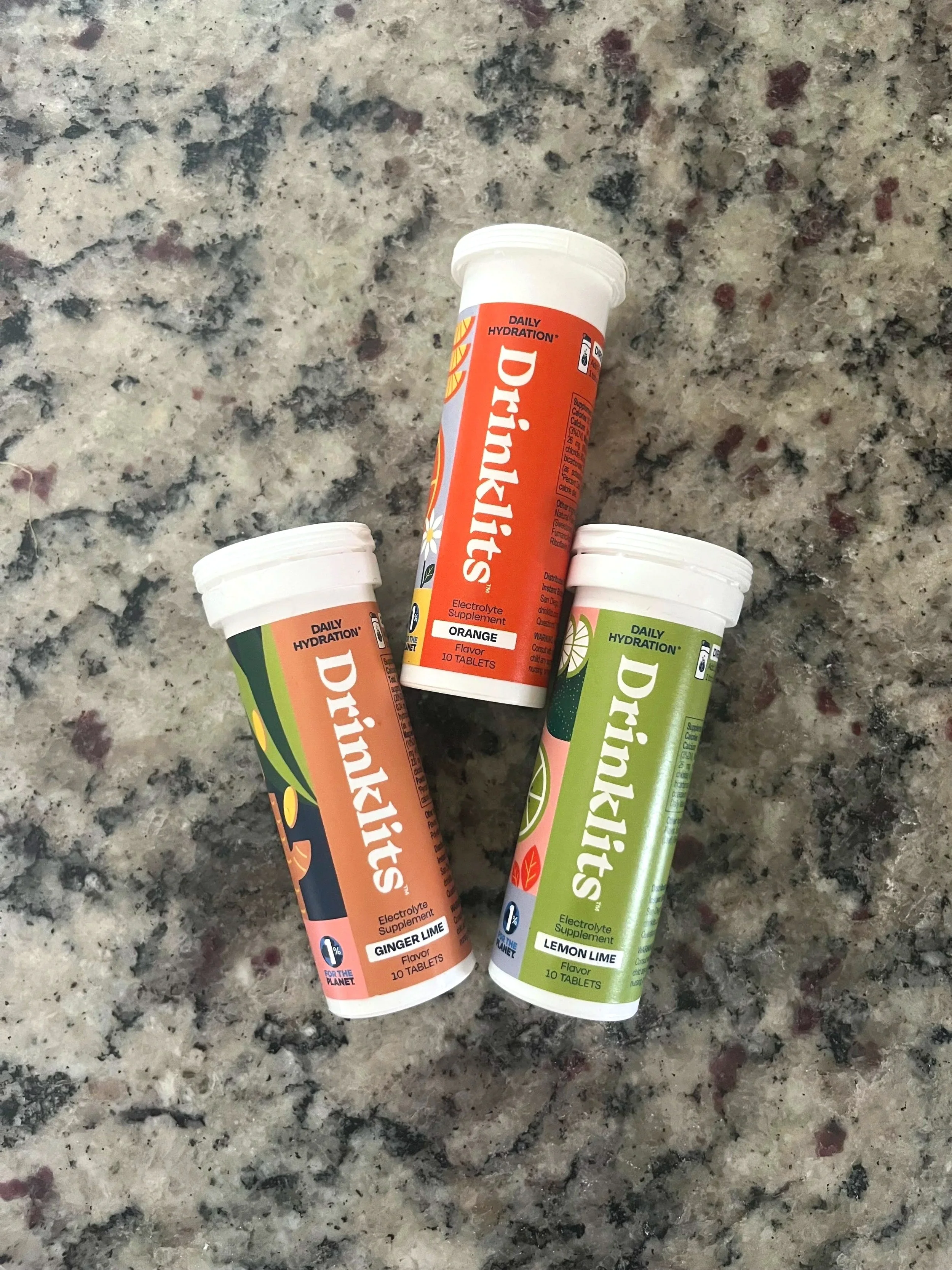 Three tubes of Drilaytits electrolyte supplements in ginger lime, lemon lime, and orange flavors on a granite countertop.