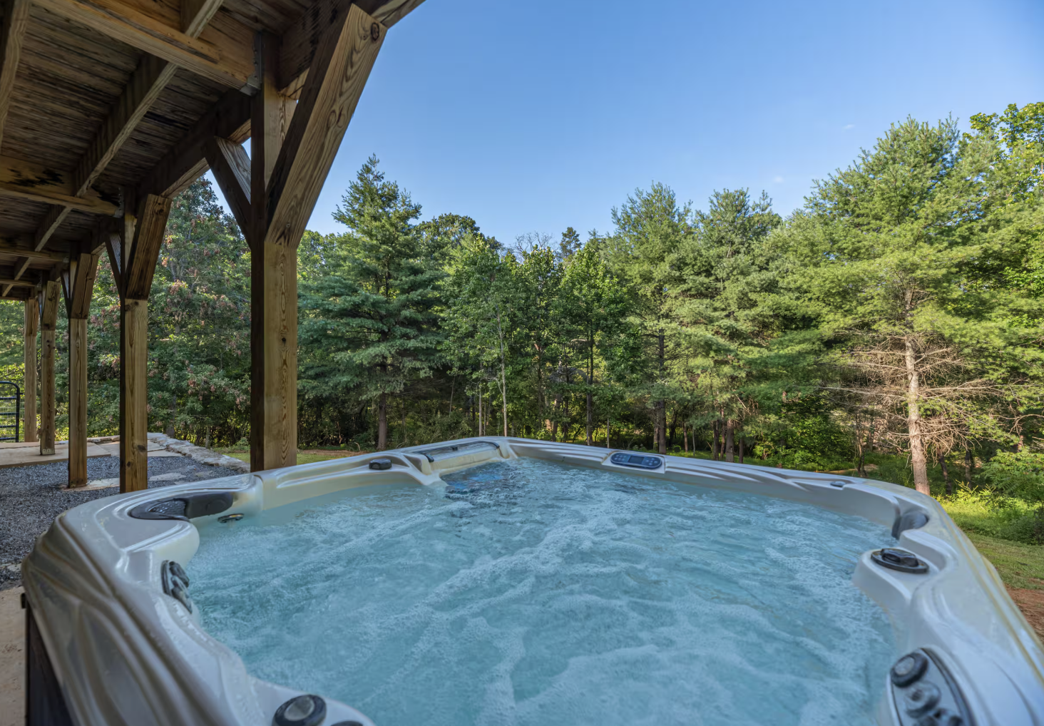 A hot tub filled with bubbling water on a wooden porch, overlooking a green forest and blue sky.