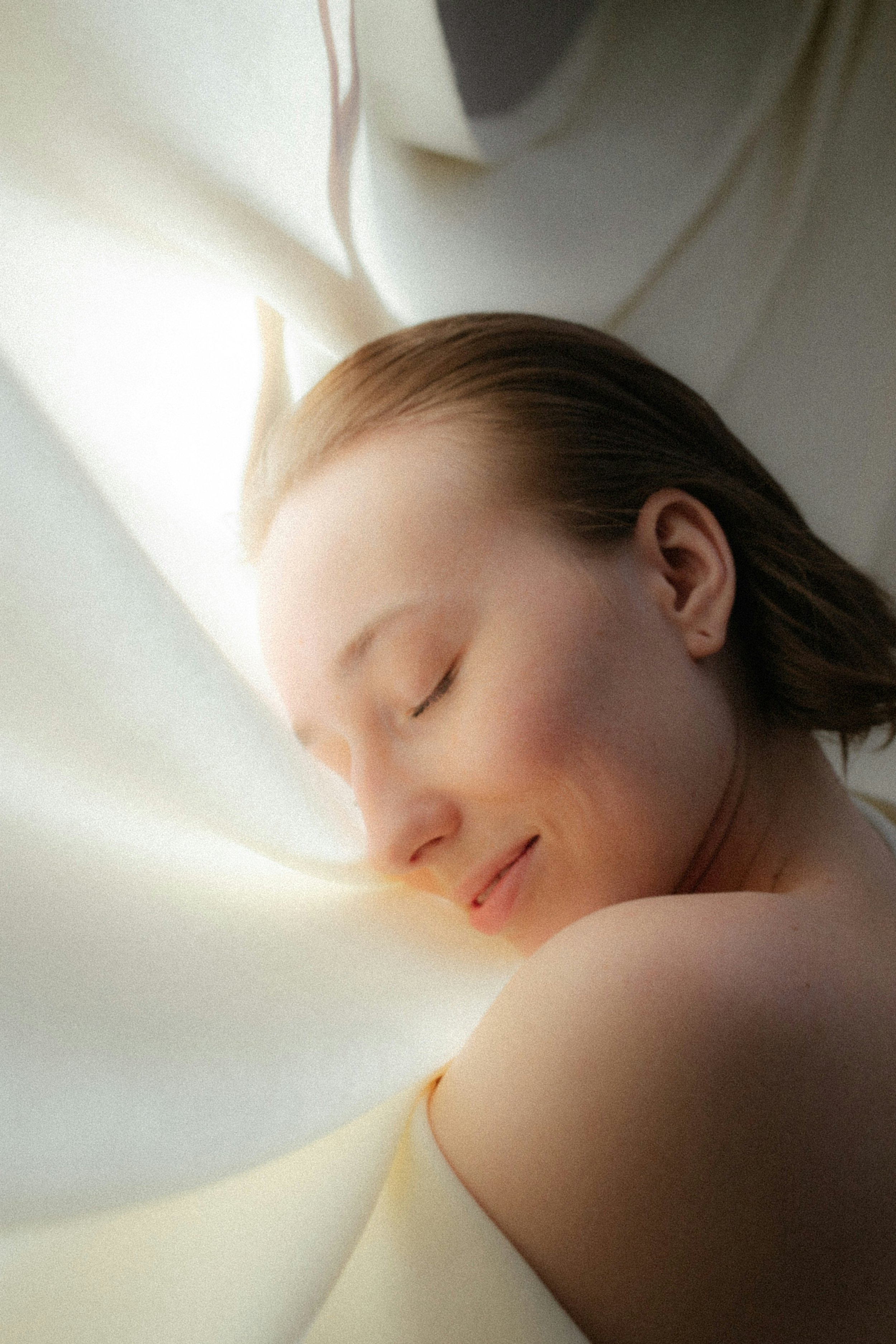 Close-up of a woman's face peacefully sleeping, with her eyes closed and lips slightly parted, resting on a pillow in a well-lit room.
