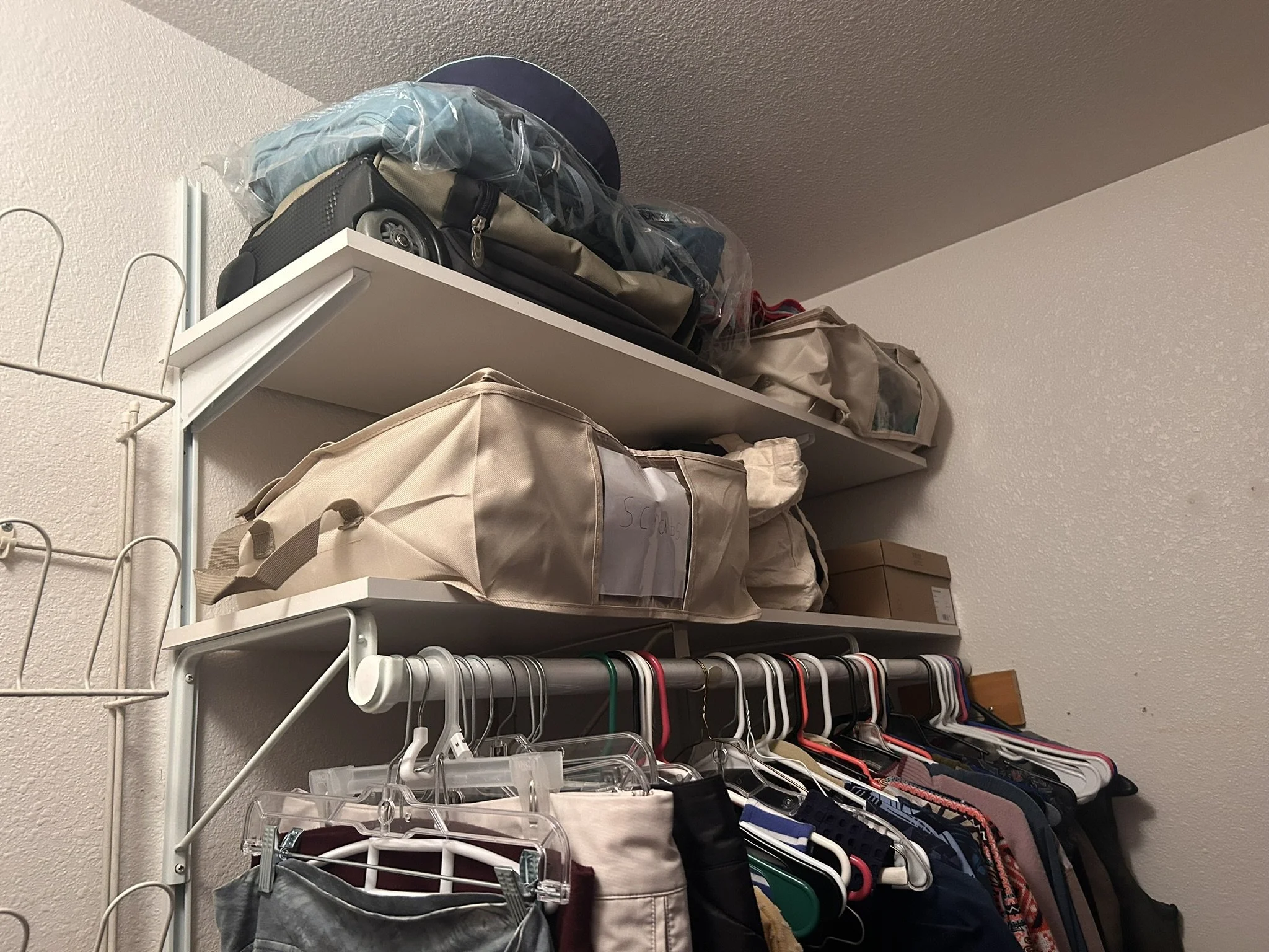 A closet on a white wire shelf with various bags, clothes, and hangers.