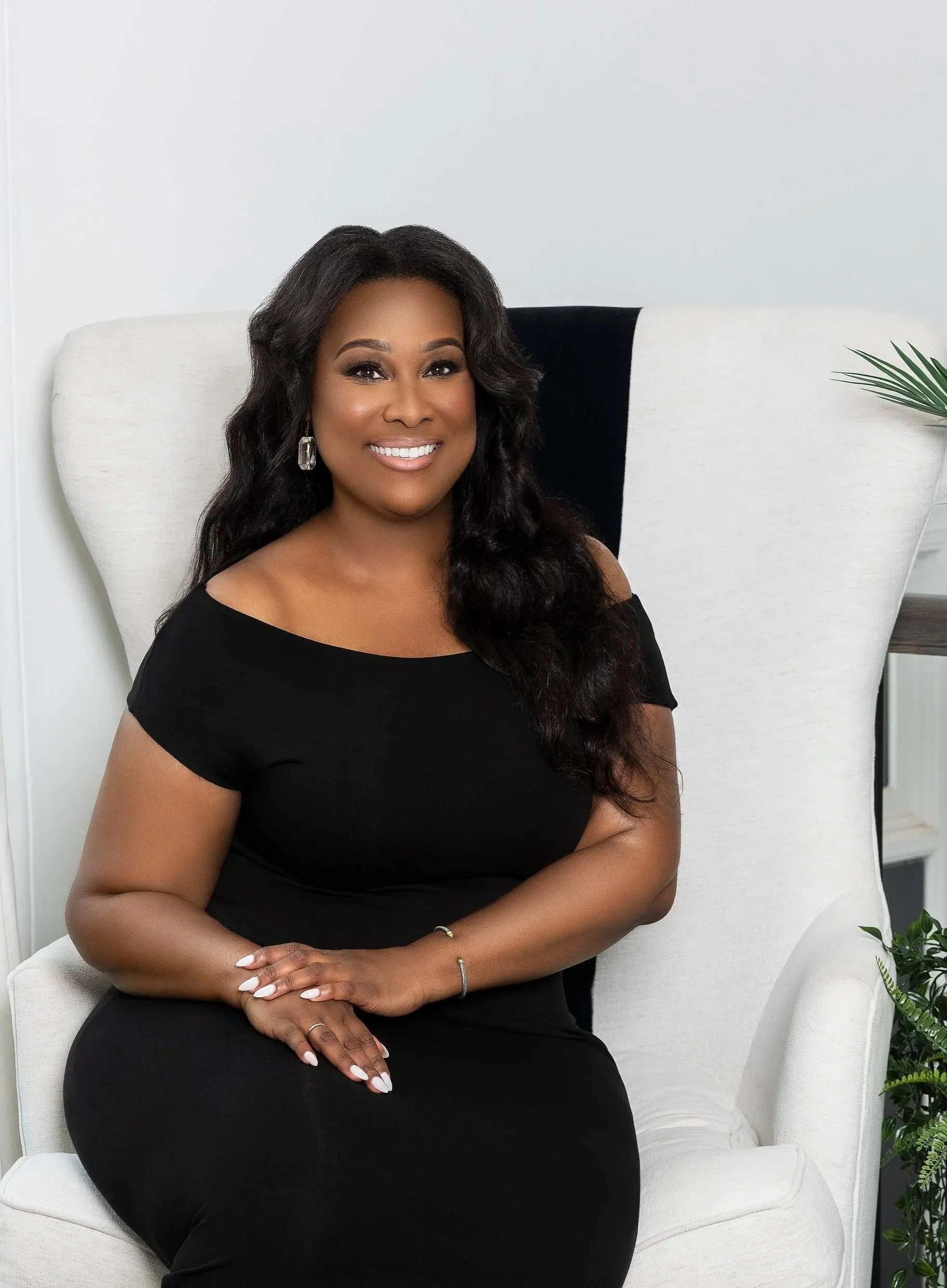 T. Lisa Gurley seated in a white chair, wearing a black dress and smiling at the camera.