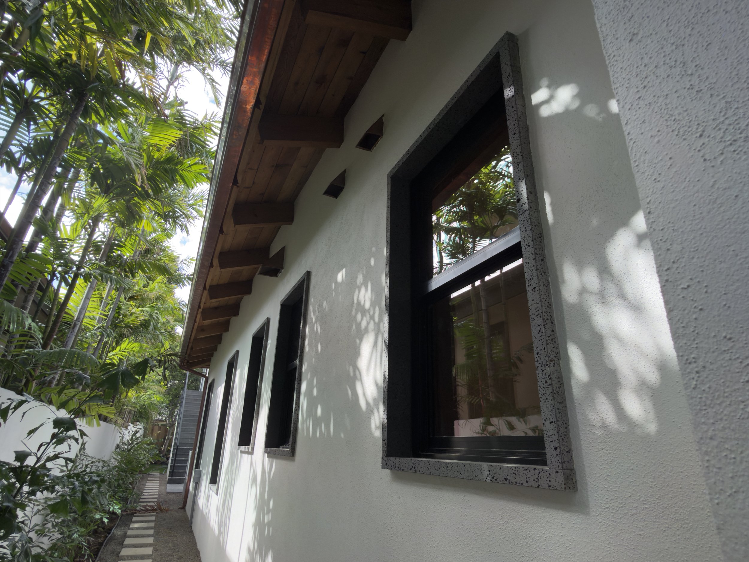 White exterior wall with black-framed windows, a wooden eaves, and lush green foliage nearby.
