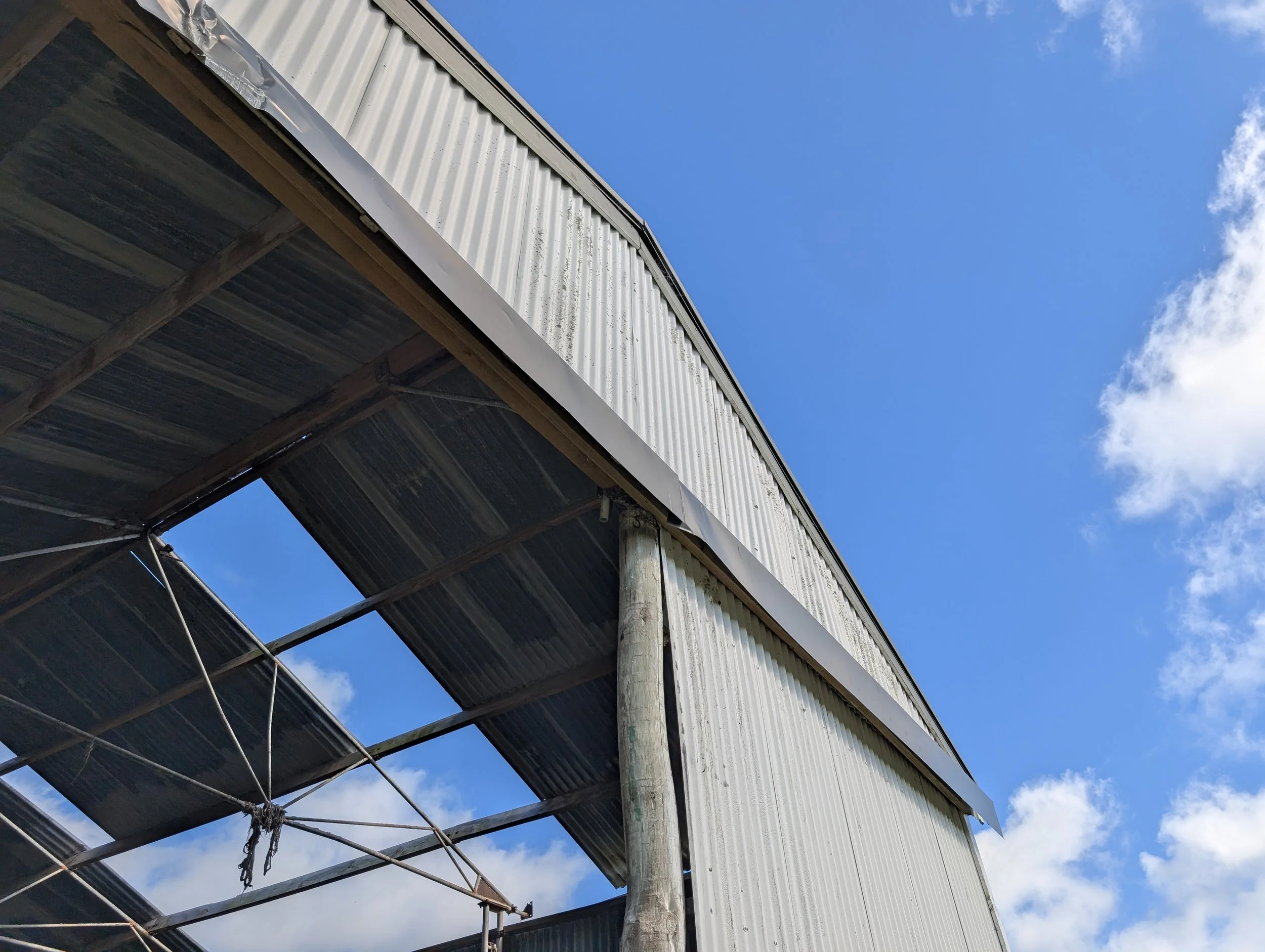 A building with corrugated metal siding and wooden supports under a blue sky with some clouds.