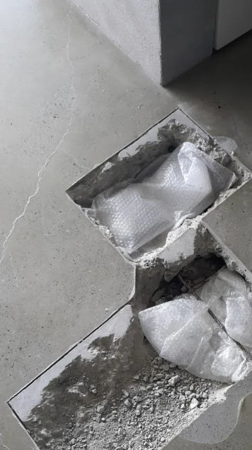 Two rectangular cutouts in a concrete floor with broken concrete debris. One cutout contains bubble wrap, and the other is empty with some rubble.