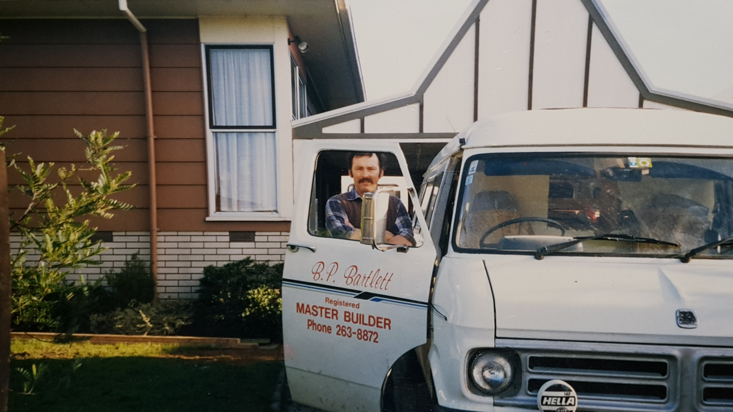 Brian standing at the open door of his white work van, with his house and garden in the background.