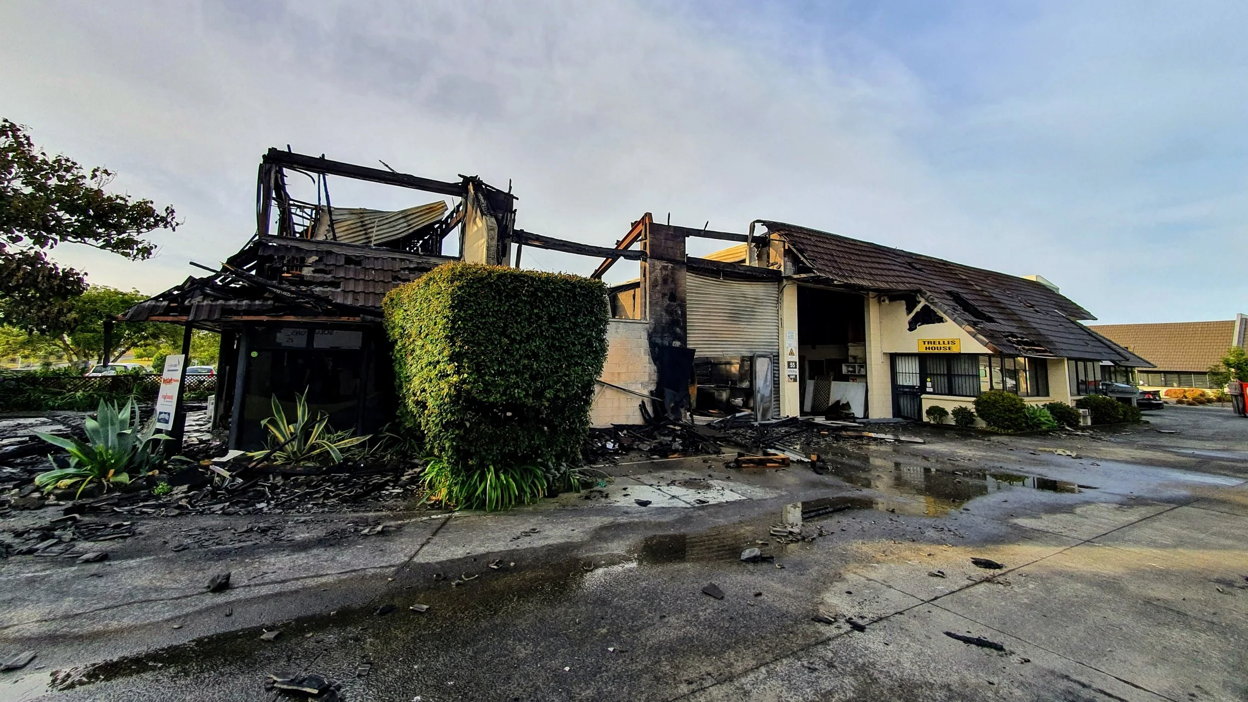 A building with extensive fire damage, charred walls, collapsed roof, and debris scattered on the ground outside.