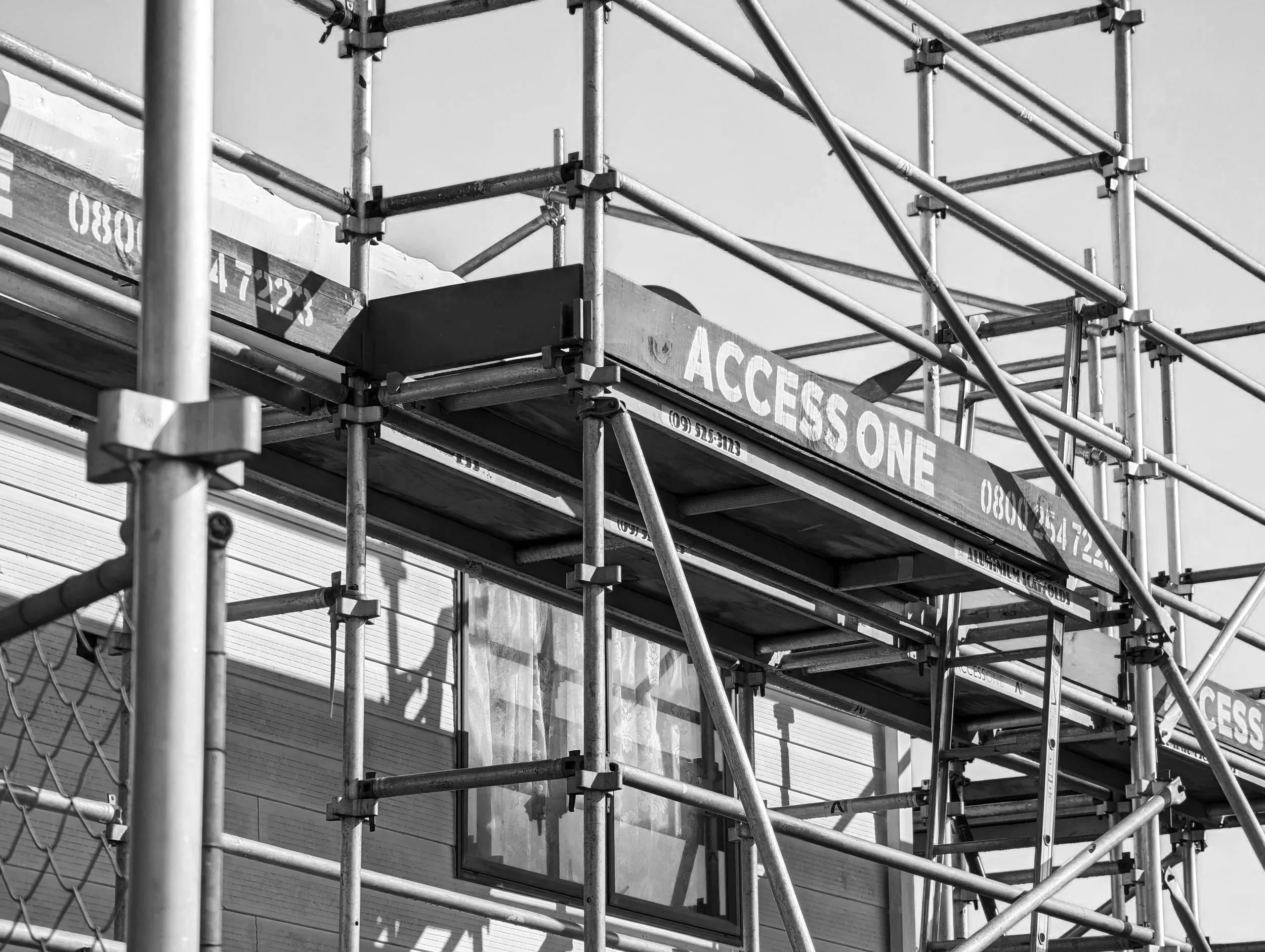 Black and white photo of construction scaffolding surrounding a building, with a sign that reads 'ACCESS ONE'.
