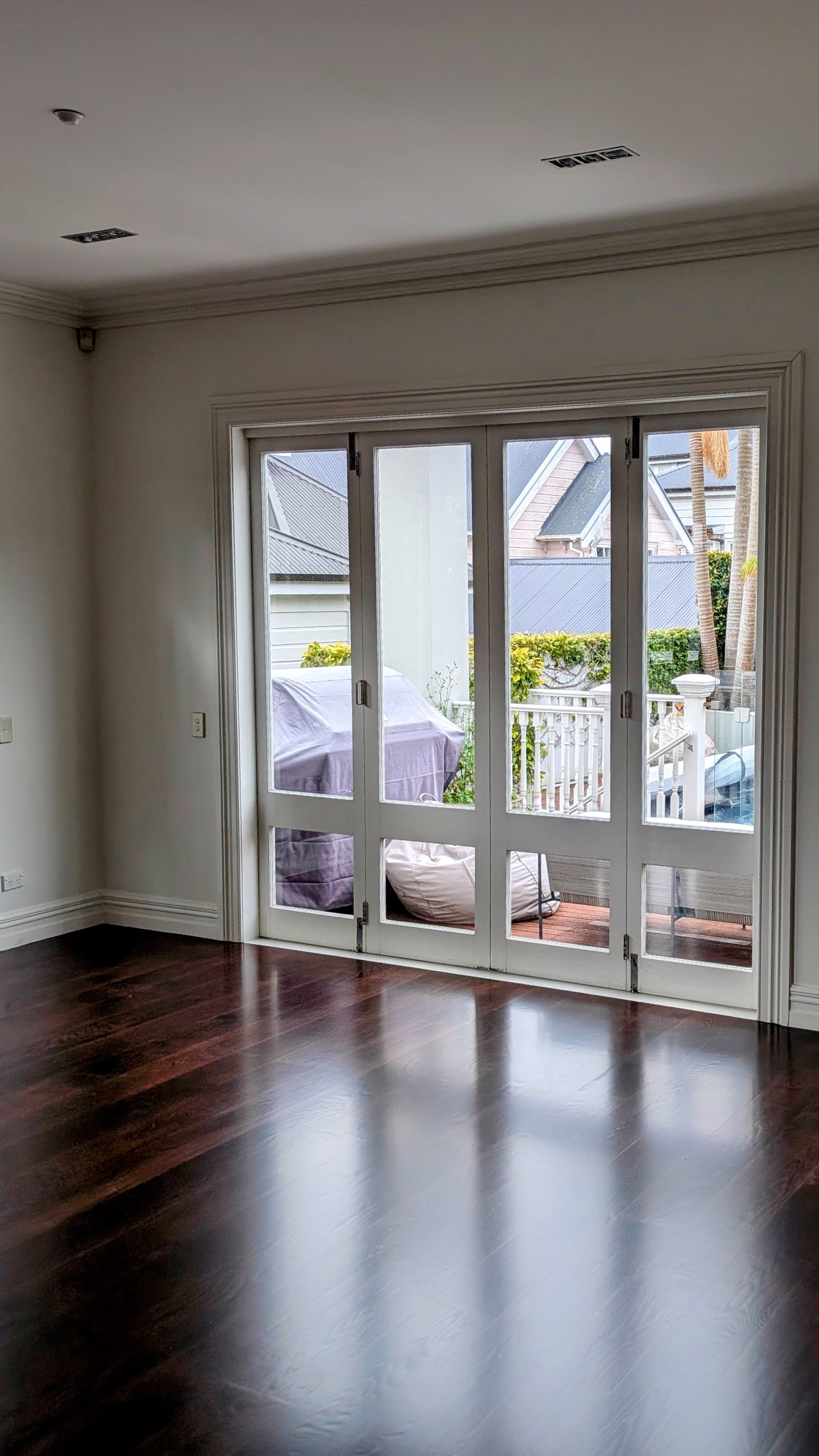 Living room with dark wood flooring and sliding glass doors leading to an outdoor patio with garden furniture and plants.